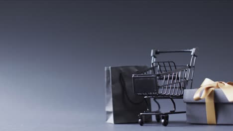 Video-of-shopping-trolley,-shopping-bag-and-gift-box-with-copy-space-over-grey-background