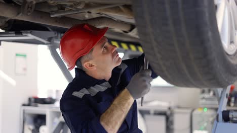 auto mechanic in helmet working underneath car lifting machine using equipment