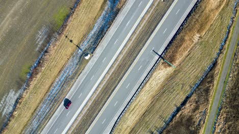 an overhead drone shot of a highway in the winter with cars passing through the frame