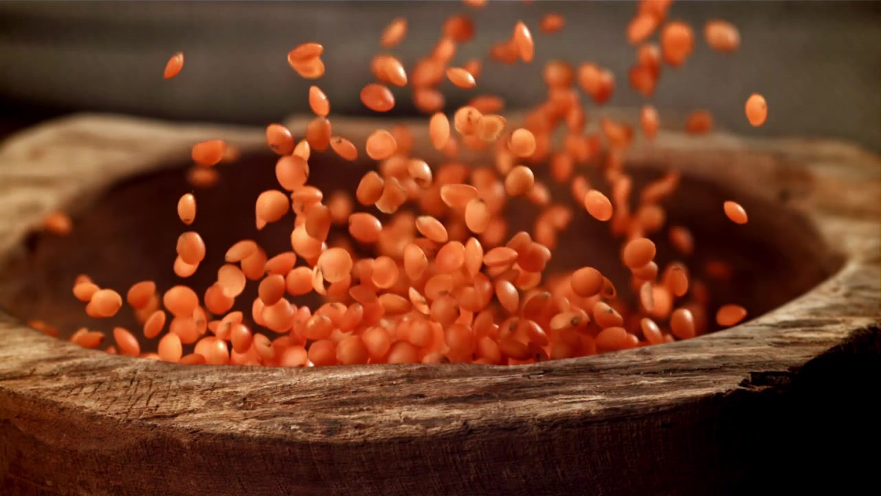 Lentilles corail tombant dans un bol en bois rustique au ralenti
