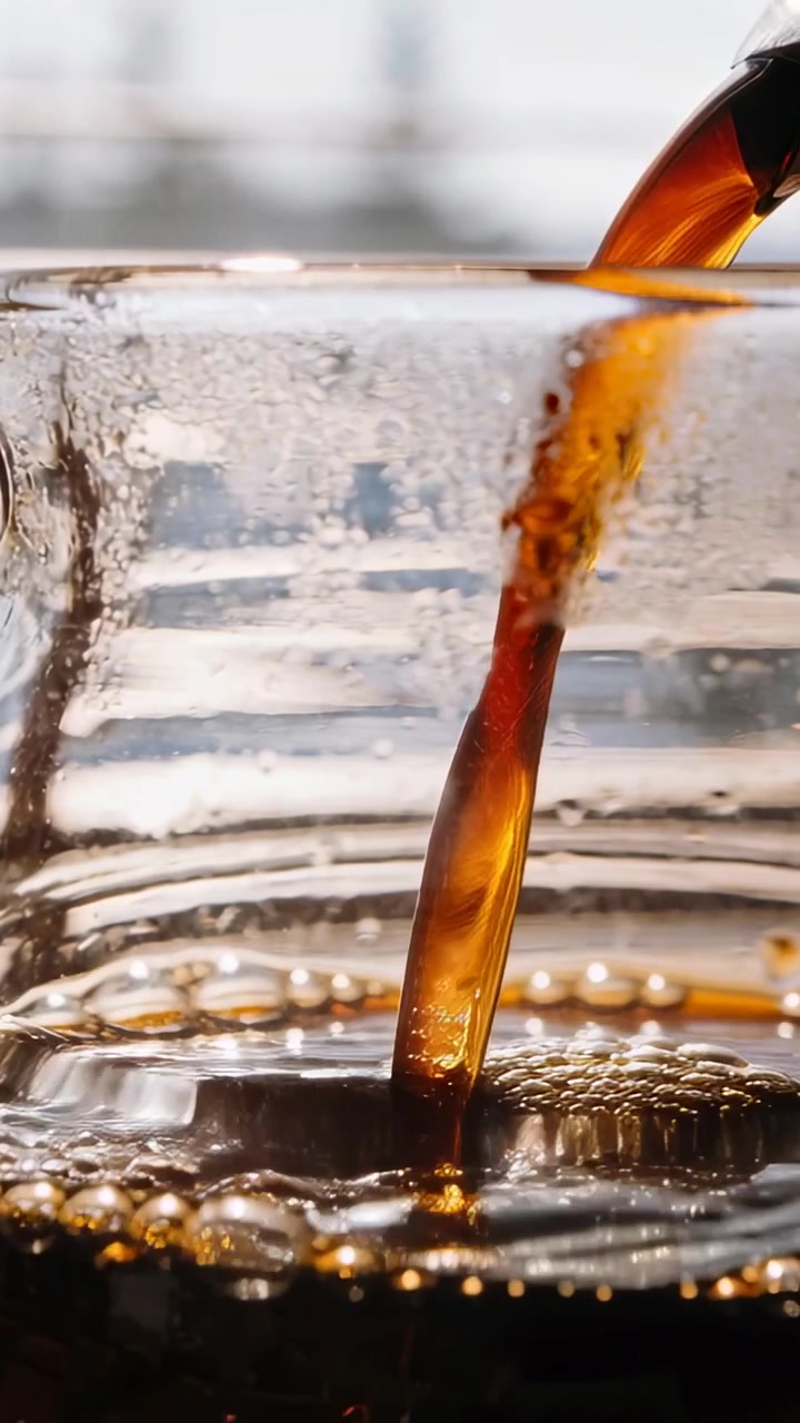 Video verticale: Beccuccio inclinato che versa liquido ambrato in un bicchiere trasparente al bancone per riempirlo di schiuma.