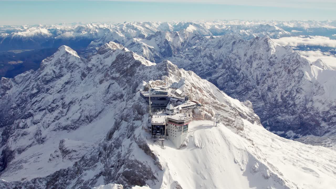 espectacular vista aérea del edificio en la cima de una cumbre nevada con los alpes desplegándose al fondo