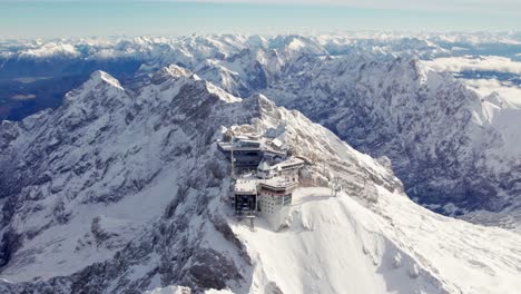 dramatic aerial of the building on top of a snowy summit with the alps unfolding in the background