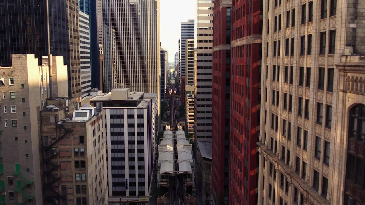 Vista drone di una stazione sopraelevata CTA e di una linea ferroviaria che attraversano un denso corridoio di grattacieli del centro di Chicago alla calda luce della sera