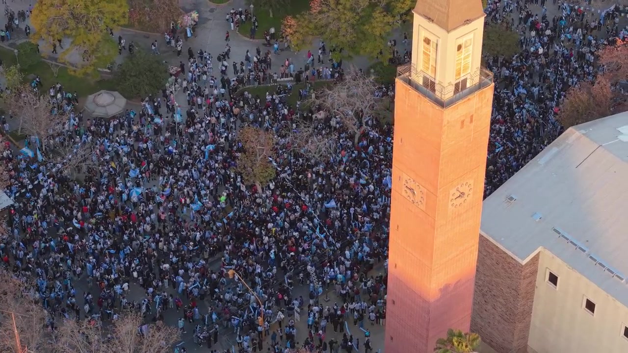 Riprese aeree con drone catturano una folla immensa di tifosi argentini in Piazza 25 de Mayo, San Juan, che celebrano con gioia la vittoria della Coppa del Mondo FIFA 2026 al tramonto, vibrante e festosa.