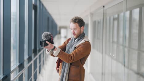 stylish man with a mirrorless camera filming a blog in the hallway of a business center