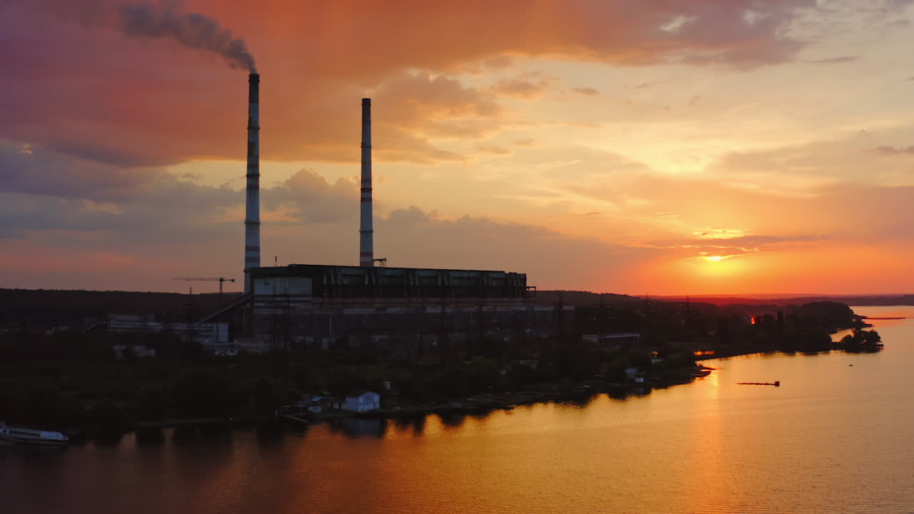 Factory on orange background. Harmful chemical plant over the river at sunset. Large territory of industrial plant in the countryside.