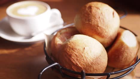 closeup of freshly baked bread rolls in a basket with a cup of coffee