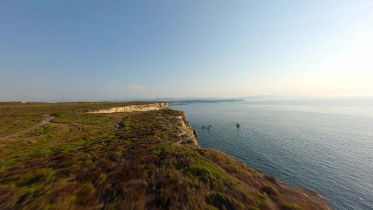 Una dinamica ripresa drone FPV che si libra sulle aspre scogliere calcaree di Cabo Peñas, il punto più settentrionale della Spagna, affacciandosi sul Mar Cantabrico durante l'ora d'oro.
