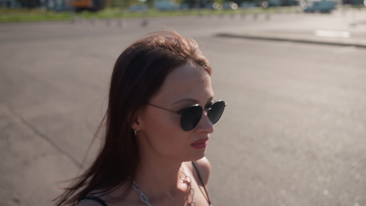 Close up of woman wearing sunglasses and chain necklace walking outdoors in sunlight, exuding confidence, urban style, independence, elegance, and modern lifestyle