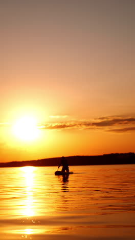 person sits on the paddle board approaching camera. sunset on the river for practicing sport. vertical video.