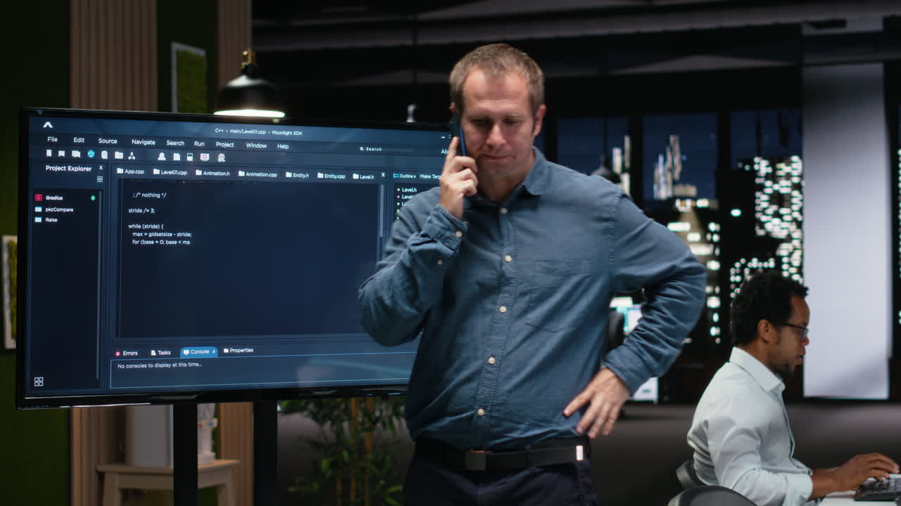 Programmer Talking on Phone While Pointing at Code on Large Screen