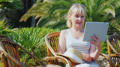 woman tourist with the tablet says he sits in a wicker chair on the background of palm trees always