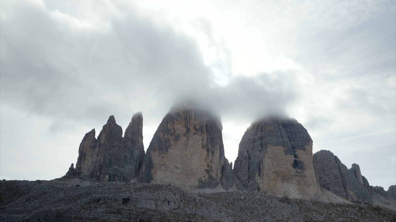천천히 상승하는 공중 촬영으로 정상 위에 구름이 있는 tre cime di lavaredo를 드러 ⁇ 니다.