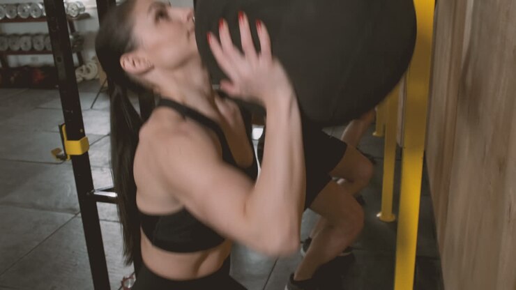 A Strong And Athletic Young Woman And Two Young Men Throwing The Medicine Ball Up In The Air And Catching It