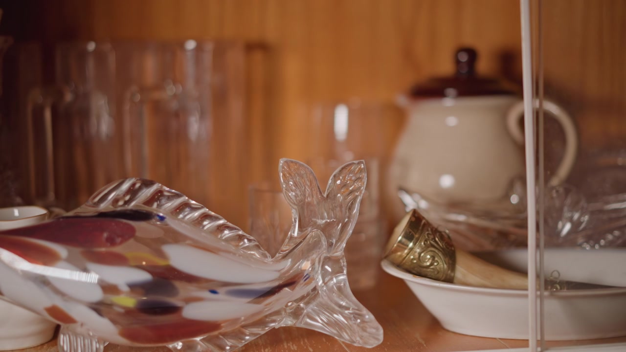 Dekorativer Glasfisch mit Vintage-Ambiente. Bunter Glasfisch auf einem Regal mit Porzellan-Akzenten. Lebendige Glasfisch-Sammlung, ausgestellt neben Porzellan-Teekanne und Schalen in nostalgischer Umgebung