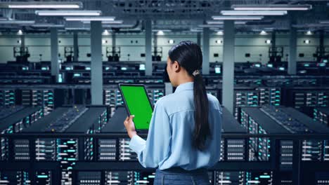 vista trasera de una mujer de negocios asiática usando una tableta con una pantalla verde simulada en el centro de datos