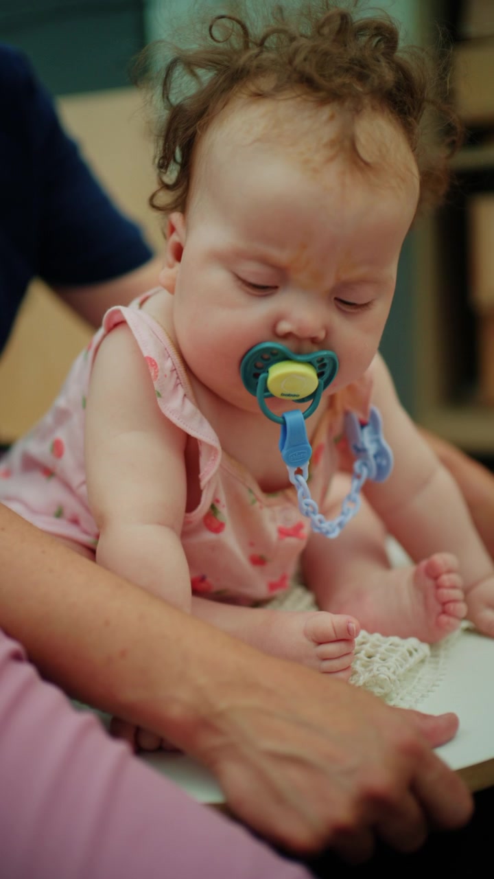 Baby sleeping peacefully with a pacifier in mouth, being held gently by a parent's hands, showing infant care and innocence