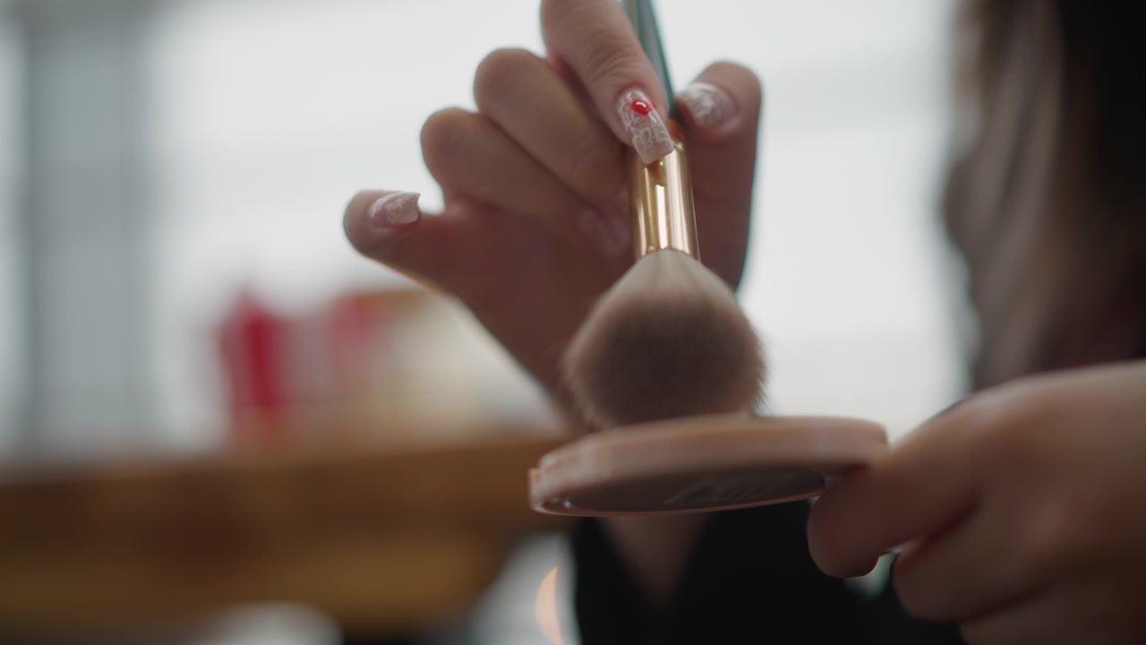 Close-up hands using fluffy makeup brush on powder compact, showing bristle splay, gentle circular movement, product pickup, soft pressure, and delicate lifting motion during beauty routine in