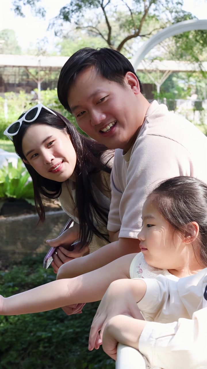 พ่อแม่และเด็กๆ ยิ้มแย้มพิงราวสะพานระหว่างการเยี่ยมชมสวนสาธารณะกลางแจ้งที่มีแดดจ้า