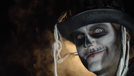 frightening man in skeleton halloween makeup turns head and looks into camera with eyes wide open