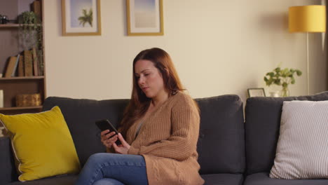 woman sitting on sofa at home at streaming or watching movie or show or scrolling internet on mobile phone 1