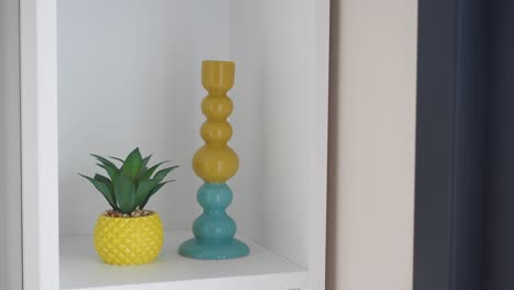 yellow and blue candlestick and succulent on a white shelf