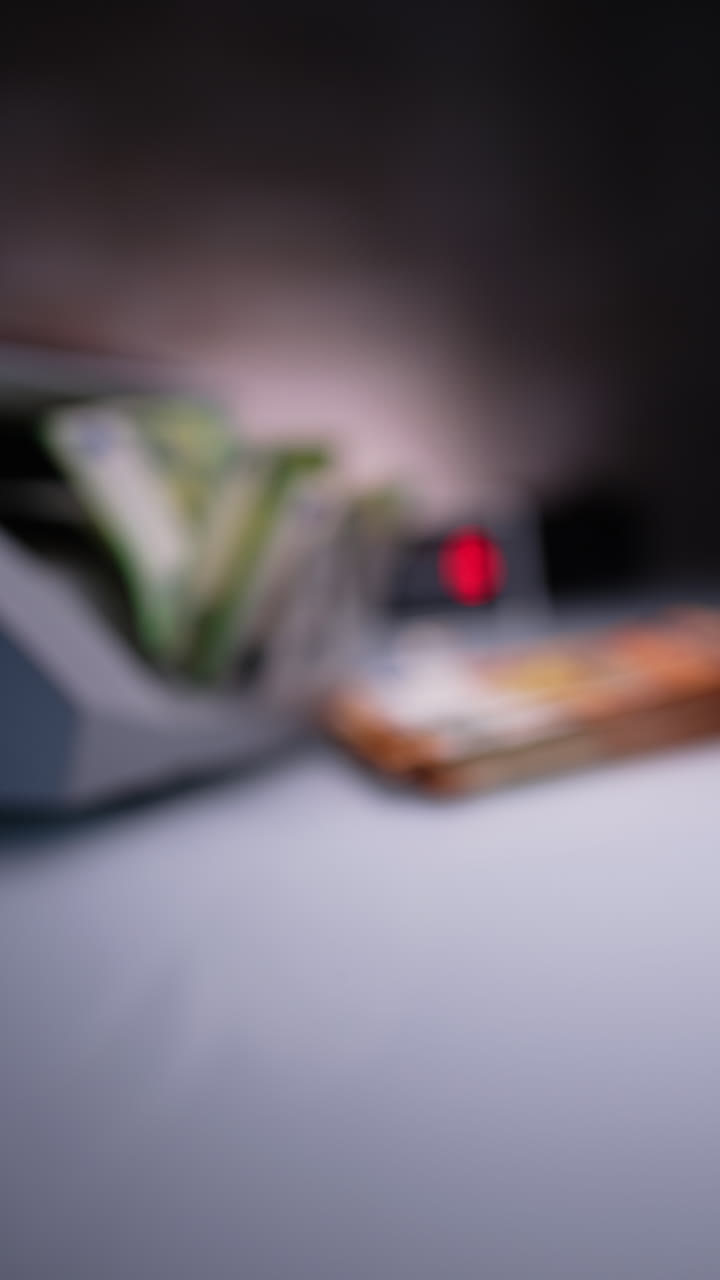 Money counting device works processing cash. Green one hundred euro bills are put on the desk. Blurred image. Close up. Vertical video.
