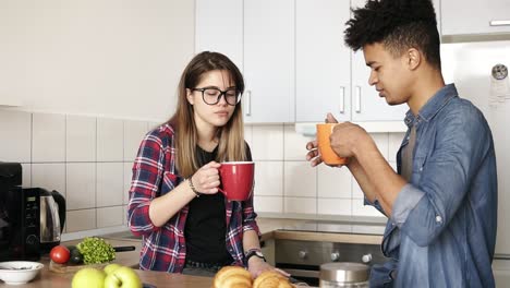 Glückliches-Paar,-Kaukasisches-Mädchen-Und-Mulatte-In-Den-Zwanzigern,-Die-Morgentee-In-Der-Küche-Trinken.