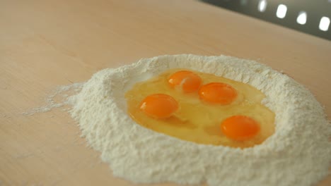 close up shot of traditional italian way tagliatelle making by pouring eggs in flour on a wooden board