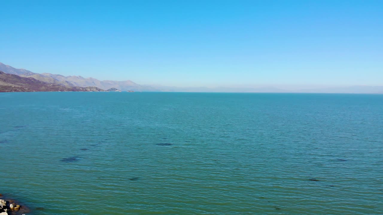 Beautiful lake with green turquoise water surrounded by mountains with rocky slopes under bright clear blue sky in Shkodra