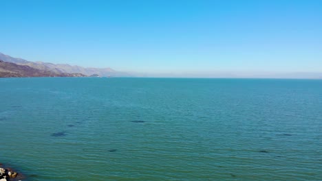 beautiful lake with green turquoise water surrounded by mountains with rocky slopes under bright clear blue sky in shkodra