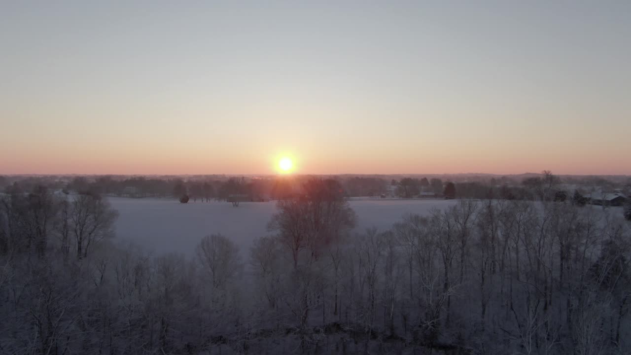 elevarse sobre el campo cubierto de nieve y los árboles para revelar el amanecer