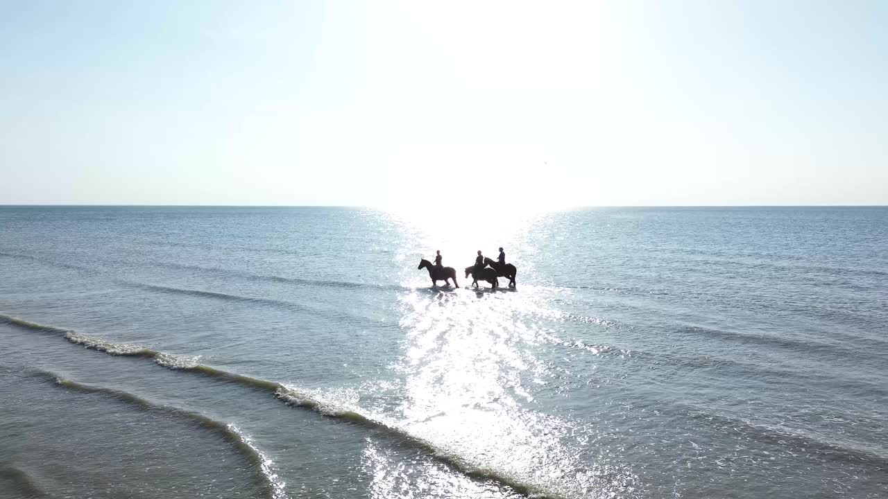 aerial footage of cavaliers riding through the tide at Deauville beach, with waves gently rolling in and golden light illuminating the scene. A perfect fusion of sport, nature, and elegance.
