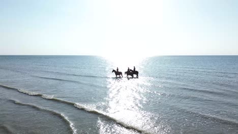 aerial footage of cavaliers riding through the tide at deauville beach, with waves gently rolling in and golden light illuminating the scene. a perfect fusion of sport, nature, and elegance.