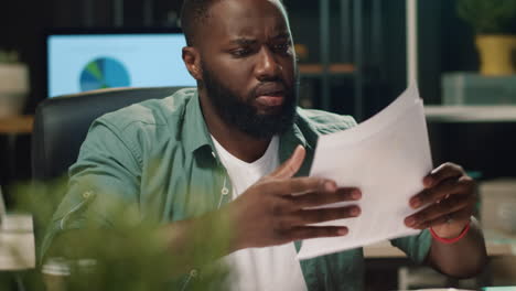 African business man reading document indoors. Annoyed afro man looking diagram