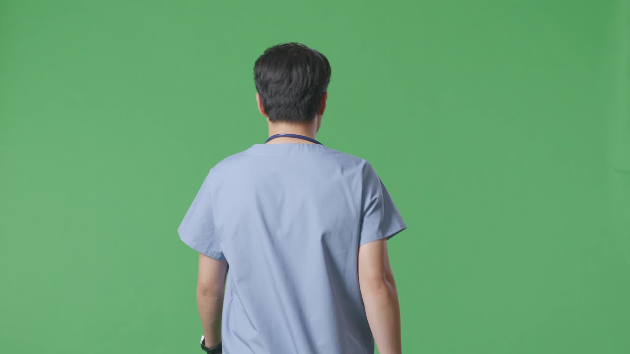 병원 에서 녹색 스크린 배경 에 걸어가는 스테토스코프 를 들고 있는 아시아 남자 의사 의 뒷면