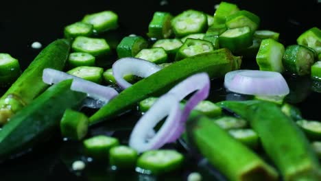 Aros-De-Cebolla-Cayendo-Sobre-Trozos-De-Okra,-Enteros-Y-En-Rodajas,-En-Un-Charco-De-Agua