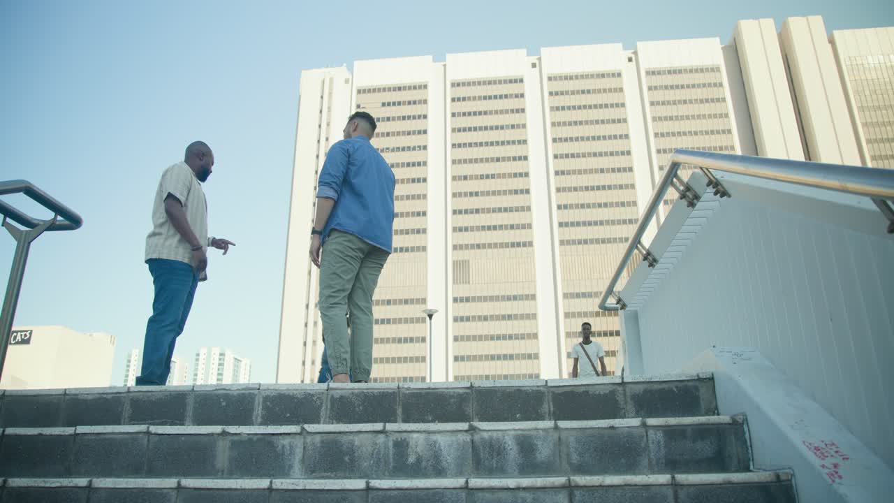Homens africanos subindo escadas na cidade, chegando ao patamar, verificando o smartphone, indo em direção ao prédio.