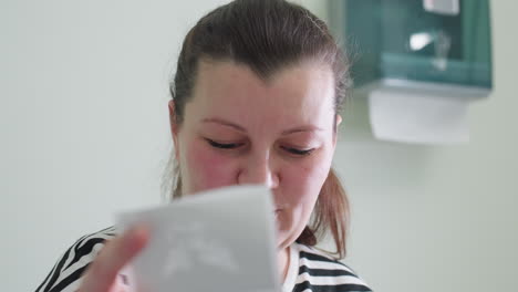 close-up of a fair-skinned woman holding her clinic visit result, smiling with approval and satisfaction as she reviews it, she seems pleased and happy with the outcome of her consultation