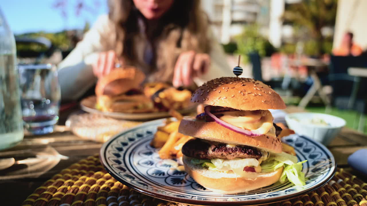 Gourmet burger served on a patterned plate in bright daylight, with blurred restaurant terrace in the background