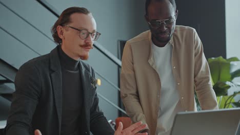 african american businessman discussing data on laptop with colleague in office