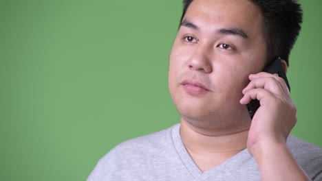 young handsome overweight asian man against green background