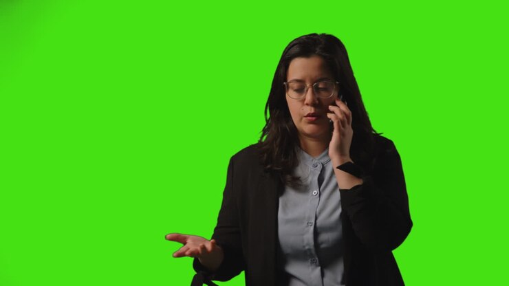 Giovane donna d'affari frustrata con gli occhiali che parla al cellulare su sfondo verde in studio 1