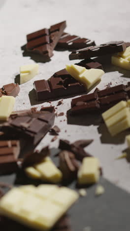 vertical video of person picking up piece from broken bars of milk plain and white chocolate