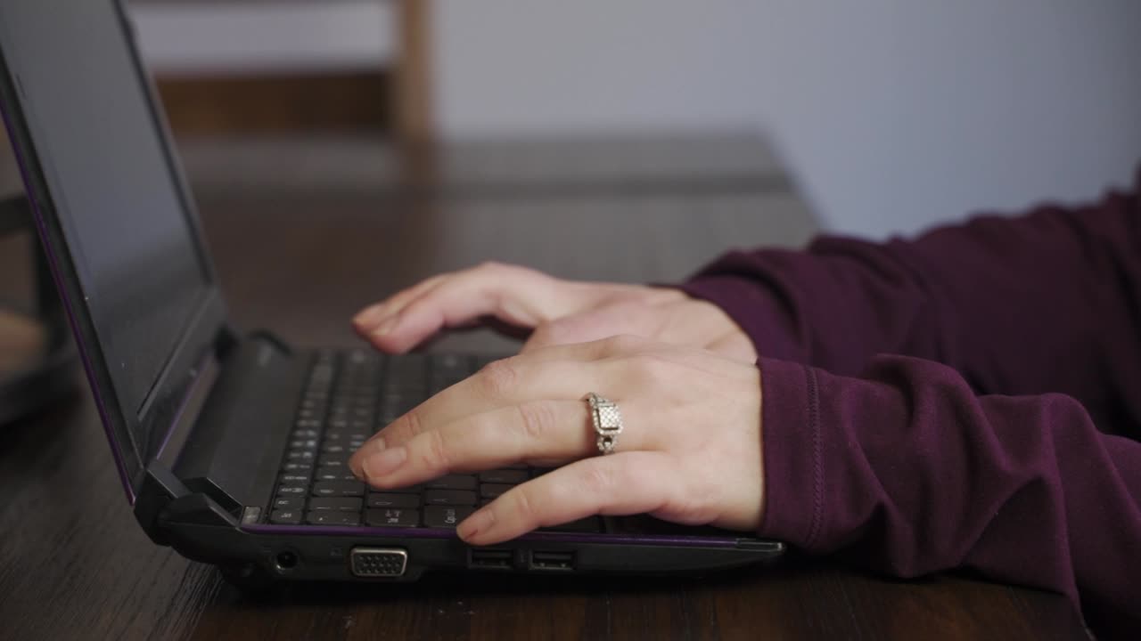 manos femeninas enfocadas con un anillo, escribiendo en la computadora portátil en la mesa del comedor en casa