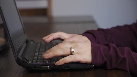 Manos-Femeninas-Enfocadas-Con-Un-Anillo,-Escribiendo-En-La-Computadora-Portátil-En-La-Mesa-Del-Comedor-En-Casa