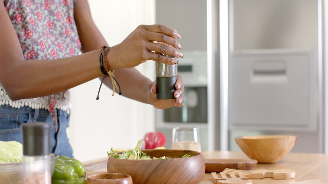 Seasoning salad, woman preparing fresh meal in modern kitchen with wooden bowls