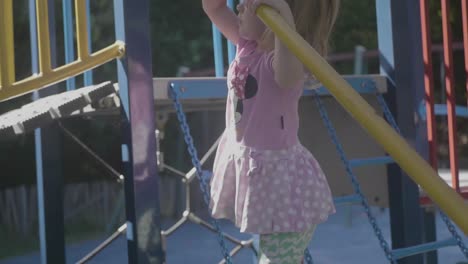 shot in slow motion of a 4 years old girl climbing a structure in a playground during a sunny day