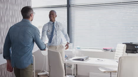 mature male patient arriving for appointment shaking hands with doctor in office